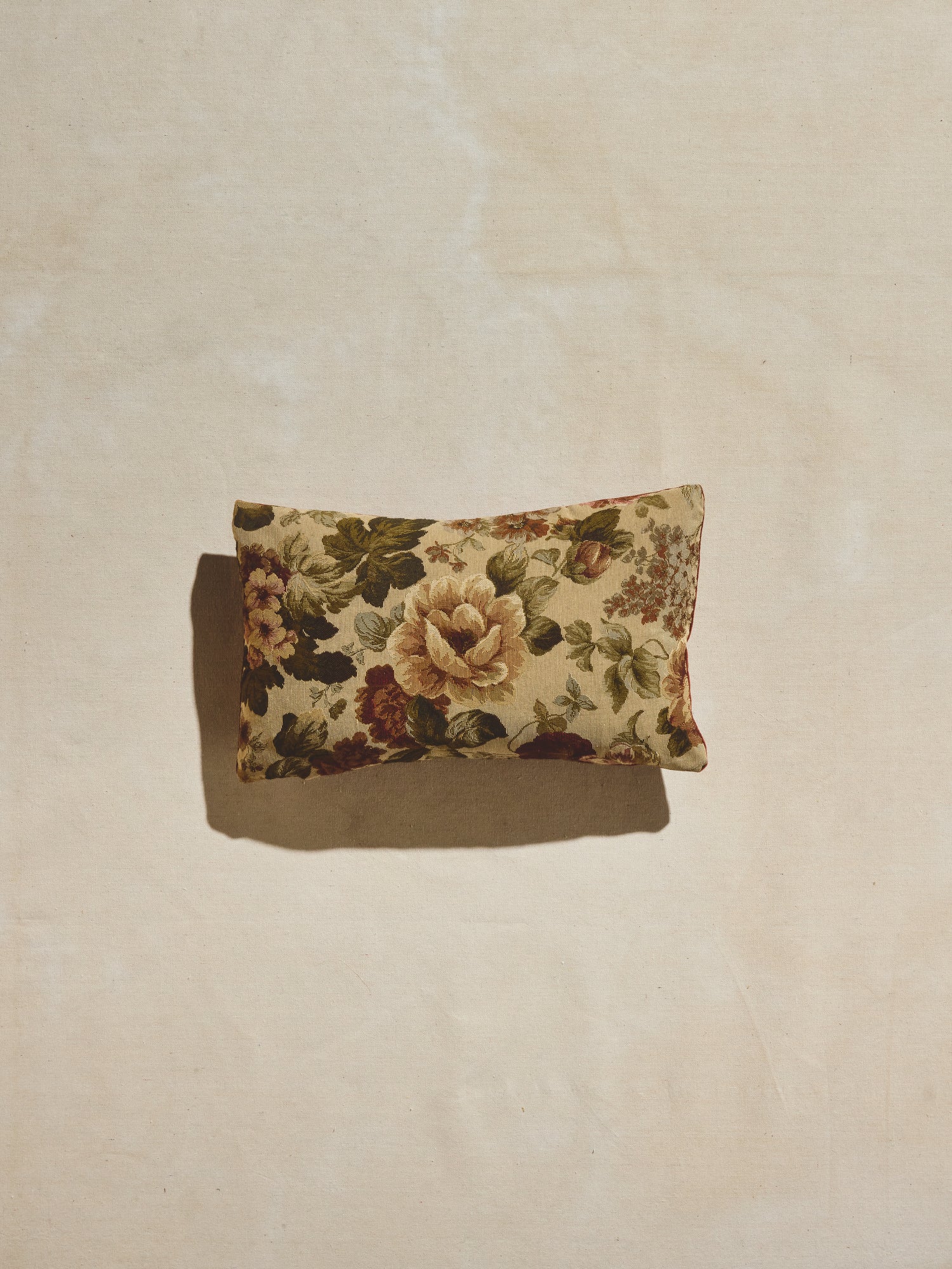 Vintage amber floral pillow with woven floral pattern in warm creams, greens, and amber tones and velvet backing in a deep rust hue.