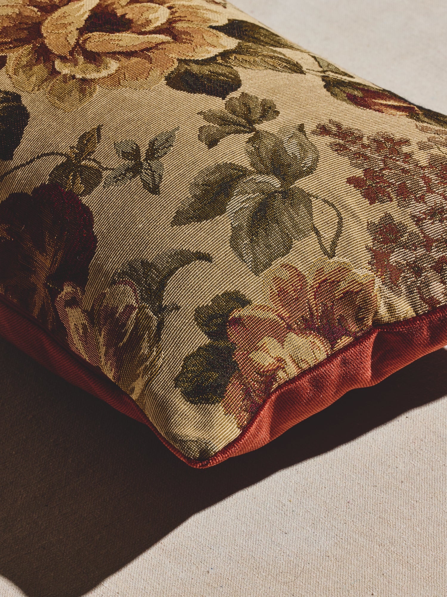 Vintage amber floral pillow with woven floral pattern in warm creams, greens, and amber tones and velvet backing in a deep rust hue.