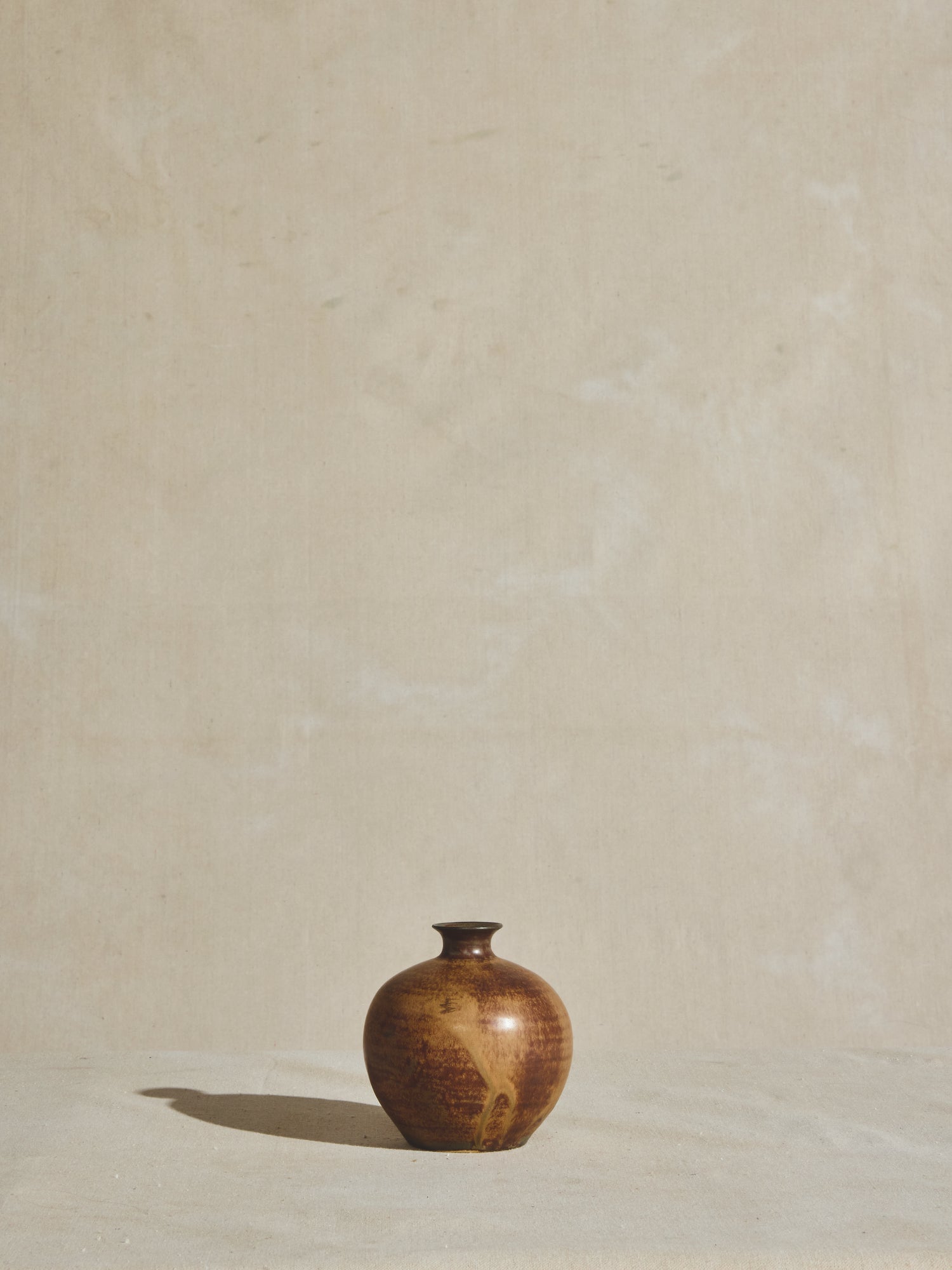 Vintage vessel with narrow neck and sphere body, glazed and aged with rust coloration.