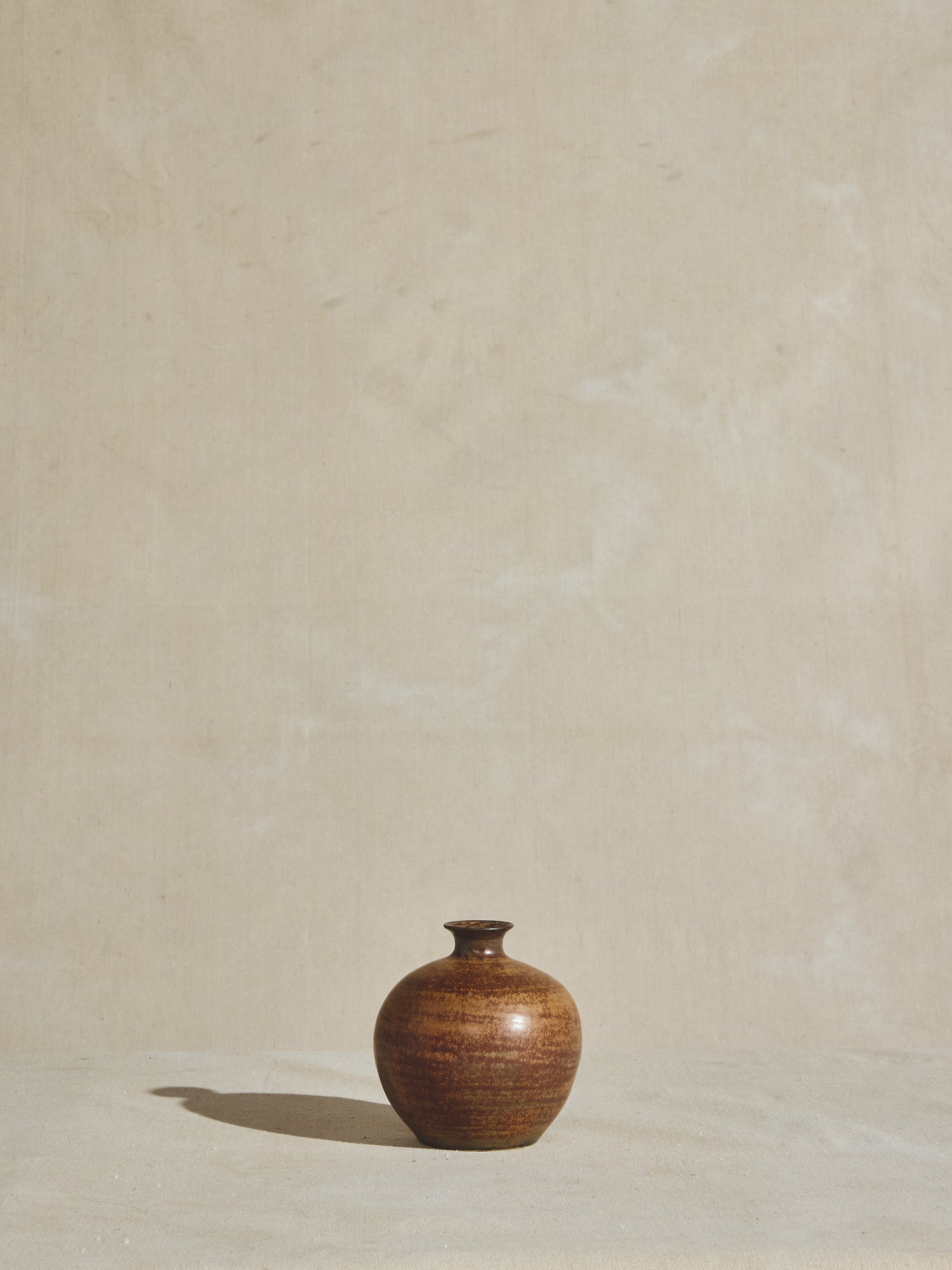 Vintage vessel with narrow neck and sphere body, glazed and aged with rust coloration.