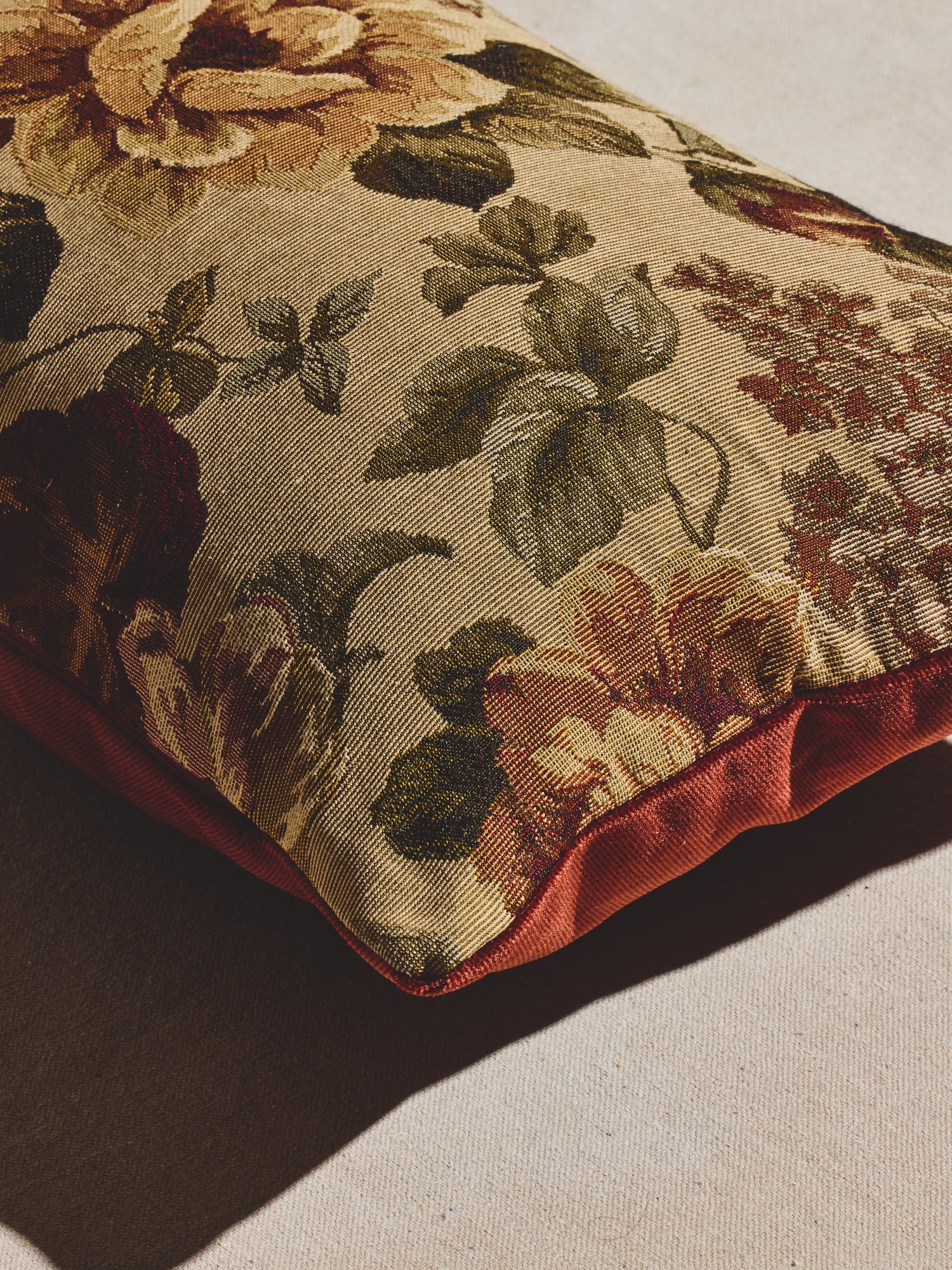 Vintage amber floral pillow with woven floral pattern in warm creams, greens, and amber tones and velvet backing in a deep rust hue. 
