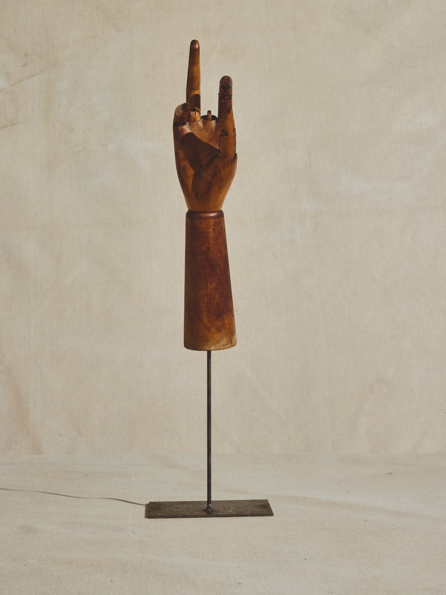 Articulated mannequin hand, missing middle finger, on metal pedestal.